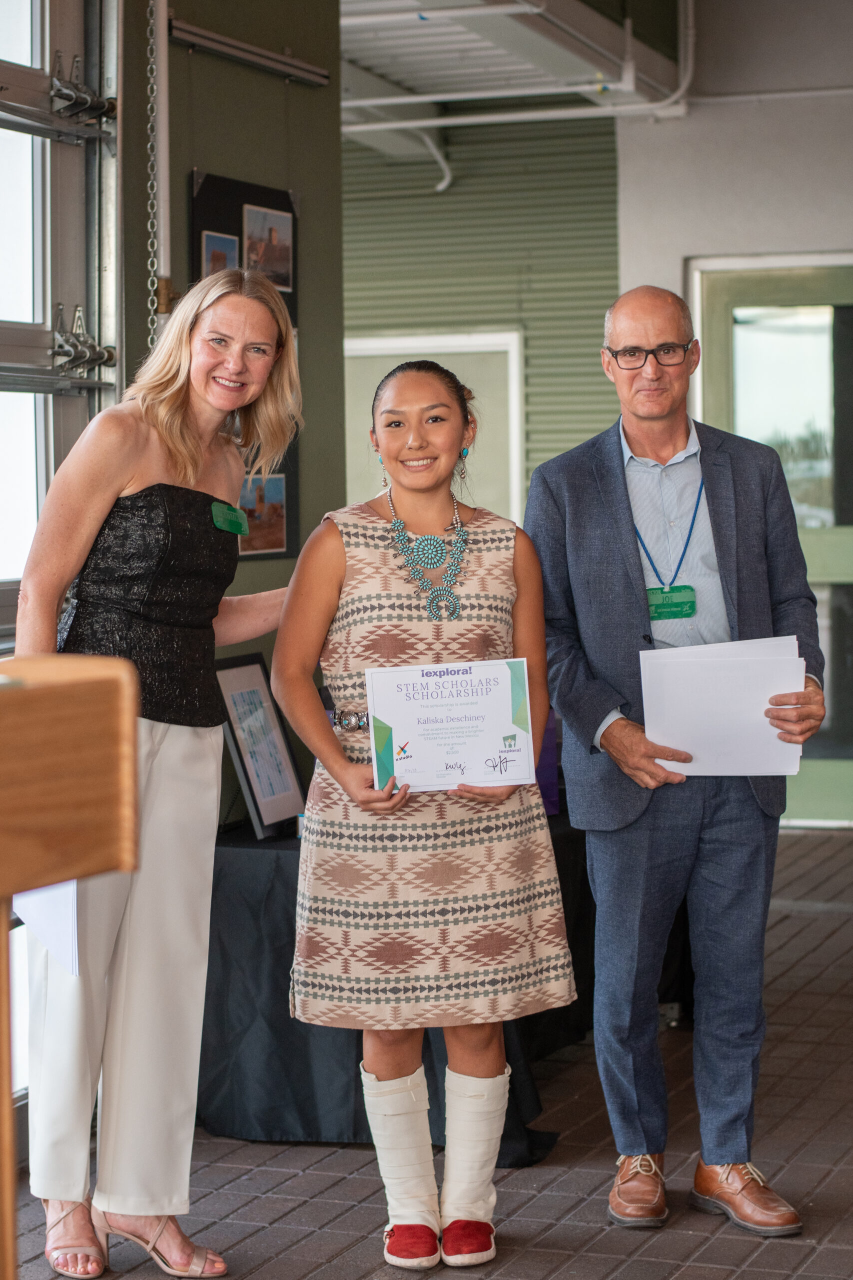 Two people award a $2,500 scholarship to a young woman in indigenous regalia