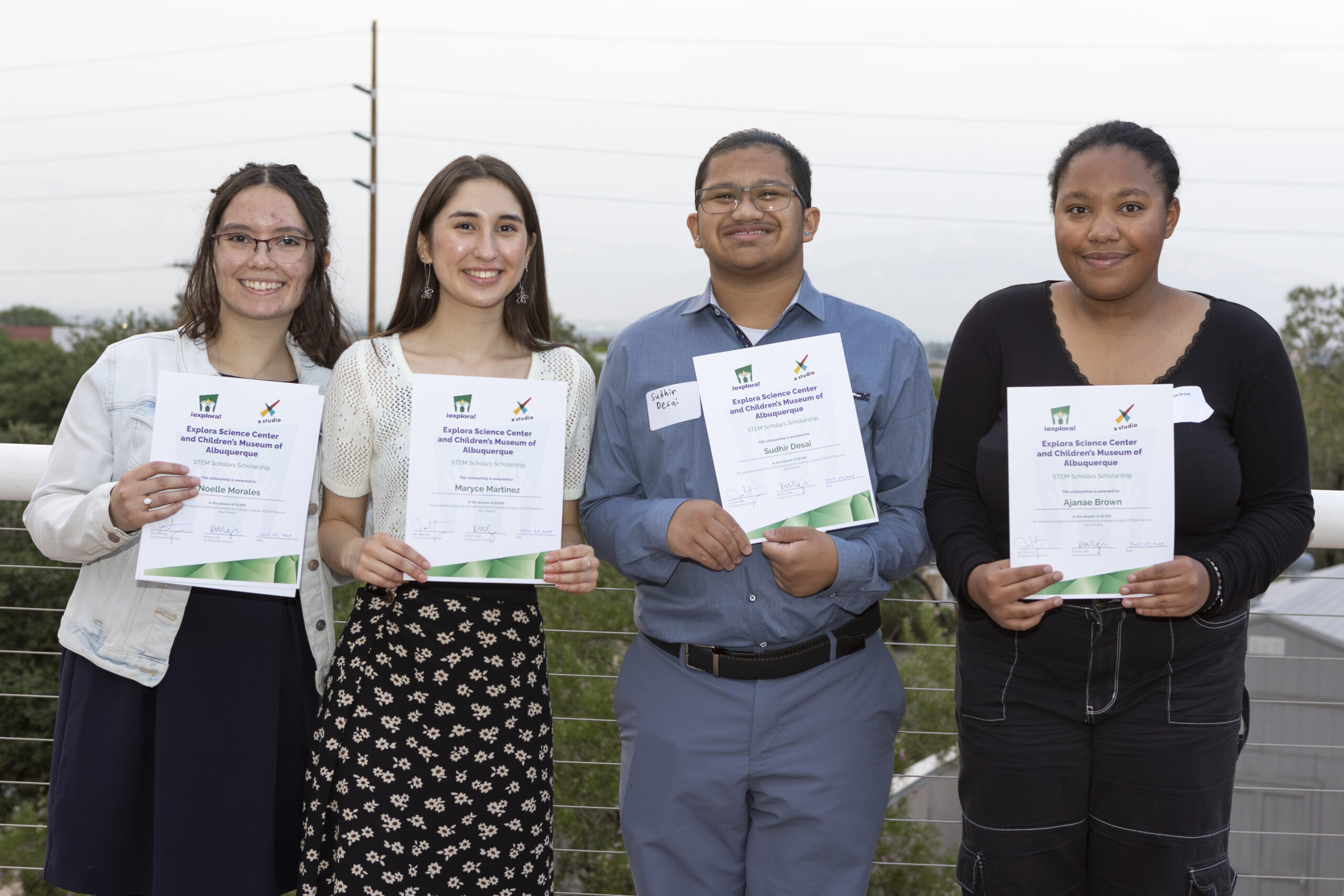 Four student awardees, one male and three female, hold their $2,500 scholarship awards up and smile for the camera