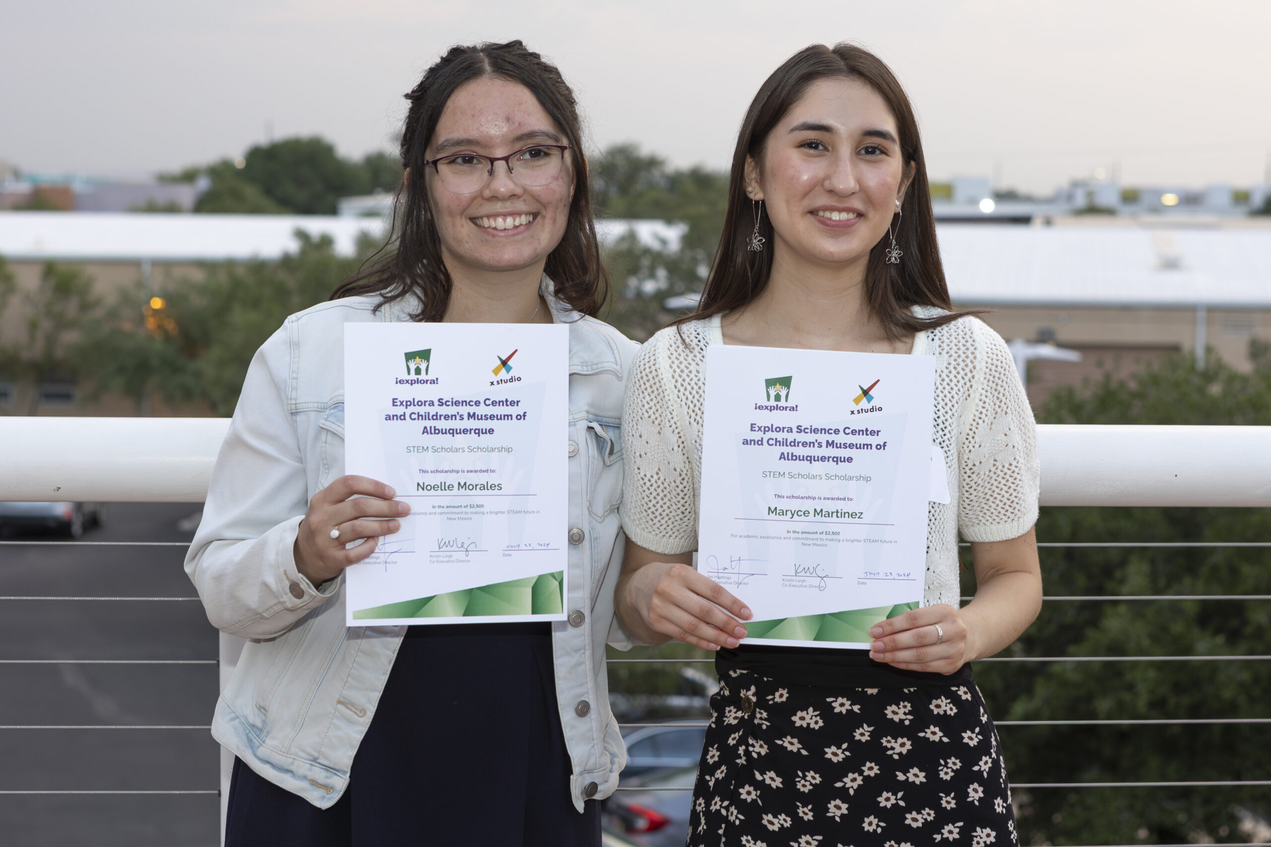 Two female scholarship awardees are holding up their $2,500 scholarship awards and smiling